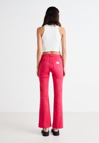 Rosa utsvingte jeans med middels høy midje og baklommer med logomerke. Kombinert med en tettsittende hvit tanktopp og svarte platå-sko.