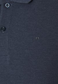 Polo texturé bleu marine foncé avec deux boutons visibles et petit logo discret brodé sur la poitrine.