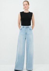 Jeans de mezclilla de pierna ancha en un tono azul claro con una cintura alta y dos bolsillos frontales, combinados con una blusa negra sin mangas con un escote redondeado.