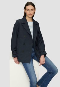 Veste double boutonnage navy avec de grands boutons, larges revers et deux poches latérales, associée à un haut rayé et un jeans bleu.