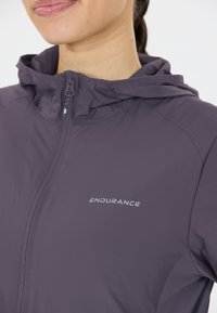Lätt lila zip-jacka med huva, med en slät yta och en reflekterande "ENDURANCE"-logotyp på bröstet.