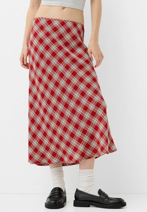 Woman wearing a red and white plaid midi skirt, white socks, black loafers, and a gray cropped top, standing against a plain white background.