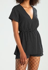 Mustapilkkuinen rompershorts, jossa on lyhyet hihat, V-pääntie ja joustava vyötärö. Yhdistetty verkkosukkiin. Pehmeä, kevyt kangas.