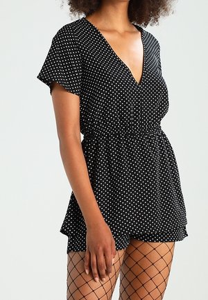 Mono negro con lunares, de manga corta, escote en V y cinturilla elástica. Combinado con medias de red. Tejido suave y ligero.