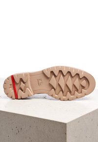 Semelle de sneaker beige clair avec de profondes rainures, dotée d'un accent rouge au niveau du talon. La texture de surface est en caoutchouc avec un design de grip structuré.