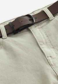 Pantalones de algodón beige claro con un cinturón de imitación cuero marrón. Costuras visibles y un cierre de botón en la cintura. Textura suave.