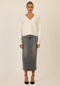 Cardigan bianco lavorato a maglia con scollatura a V e tre bottoni, abbinato a una gonna midi in denim grigia con un sottile motivo a pois e tacchi neri.