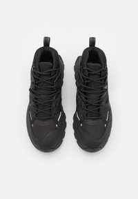 Zapatos de senderismo negros con un upper texturizado, cuello acolchado y puntera reforzada. Presentan cordones negros y acentos reflectantes a lo largo de los lados.
