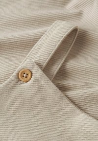 Beige textured fabric with a ribbed design, featuring a light brown button on a strap. Close-up view highlighting material details.