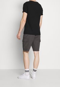 T-shirt noir à manches courtes associé à un short cargo gris foncé avec des poches latérales, porté avec des baskets blanches et des chaussettes rayées.