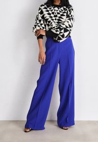 Pull en tricot à motif géométrique noir et blanc associé à un pantalon large taille haute bleu royal. Sandales noires à lanières aux pieds.