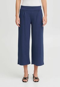 Pantalons larges navy avec une taille élastique et des plis, fabriqués en tissu doux, présentant une texture lisse et une coupe au niveau des chevilles.