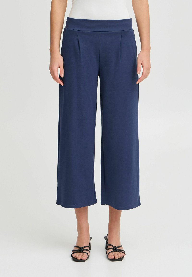 Pantalons larges navy avec une taille élastique et des plis, fabriqués en tissu doux, présentant une texture lisse et une coupe au niveau des chevilles.