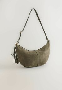 Sac besace demi-lune en daim vert olive avec bandoulière réglable, ferrures dorées, fermeture éclair et détail pompon sur fond uni.