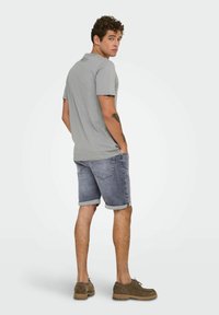 Polo gris de manga corta combinado con pantalones cortos de denim enrollados. El conjunto presenta un corte relajado y unos zapatos marrones resistentes.