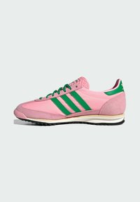 Sapatilha desportiva rosa com riscas verdes, materiais em camurça e sintéticos, língua texturada, entressola branca e sola preta com detalhes de tração.