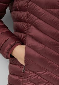Burgundská péřová bunda s designem ve tvaru šípu, zipovou kapsou a elastickými manžetami. Hladký, lehký materiál s prošívanou strukturou.