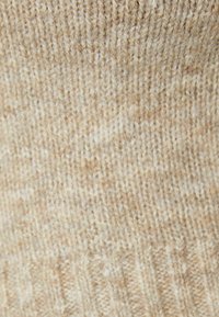 Stickad tyg i beigetoner med en texturerad mönster och mjukt, fint garn. Något varierade nyanser skapar visuell intresse.