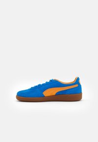 Blue suede sneaker with orange stripe accents and brown rubber sole, shown from the side on a white background.