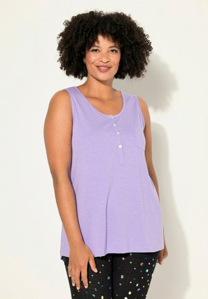 Canotta lavanda in tessuto morbido, con scollatura rotonda, taschino frontale e dettagli con bottoni. Indossata con pantaloni neri con motivi luccicanti.