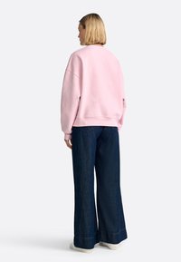 Lichtroze oversized sweatshirt met een ronde hals, gecombineerd met wijdvallende donkerblauwe spijkerbroeken en witte sneakers.