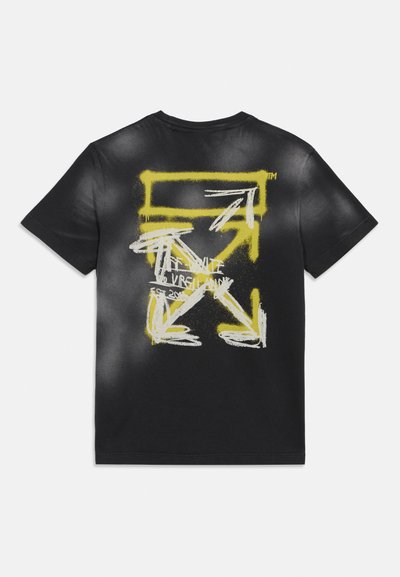 Schwarzes T-Shirt mit gelb-weißen, sprühgesprühten Pfeilen, die ein X und einen rechteckigen Rahmen bilden, mit teilweise sichtbarem Text in der Mitte.