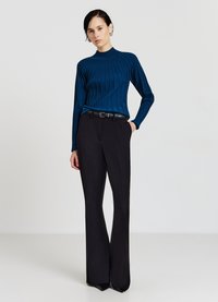 Blaues Rippstrickoberteil mit hohem Kragen, kombiniert mit schwarzen, hoch taillierten Hosen. Die Schuhe haben eine spitze Zehe. Schmale Passform mit elongated Silhouette.