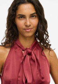 Bordo halter top izrađen od glatkog materijala, s vezanjem u mašnu oko vrata i izrezom u obliku ključa, s mekom, lepršavom teksturom.