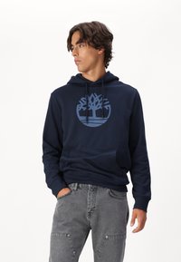 Sweatshirt bleu marine en coton, avec un grand logo d'arbre bleu clair sur le devant, une poche kangourou et une capuche à cordon.