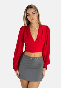Top rosso corto con scollatura a V profonda e dettagli plissettati, abbinato a una mini gonna grigia aderente con una cintura con fibbia argentata.