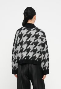 Czarny i szary sweter w kratę houndstooth o kroju krótkim, z miękkiego, puszystego materiału, z wysokim kołnierzem i szerokimi rękawami. Gładki, czarny dół.
