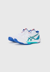 Baskets de sport blanches avec des accents bleus et verts, dessus texturé, lacets élastiques et panneau latéral à motifs. Conçues pour la performance et le confort.