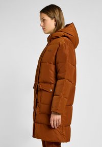 Brun, polstret vinterjakke med hætte, der har en frontknaplukning og to sidelommer. Glat tekstur, midtlængde design.