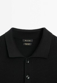 Polo noir avec un motif texturé, col côtelé et patte de boutonnage à trois boutons. L'étiquette indique "Massimo Dutti", fabriqué en coton extra-fin.