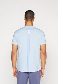 Camiseta de manga corta en azul claro con corte recto, que presenta un logo vertical blanco de "BORG" en la parte posterior y una textura suave y lisa.