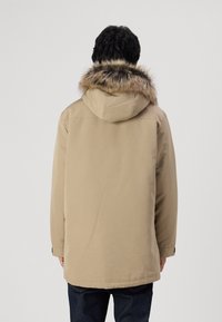 Parka marrone con cappuccio foderato in pelliccia, dotata di un taglio dritto, maniche lunghe e una texture di tessuto morbido.