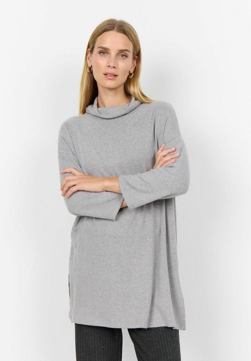Light gray, cowl-neck tunic with long sleeves, soft texture, side slits, and relaxed fit, paired with striped dark pants.