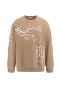 Ruda, apvalios apykaklės megztinis, pagamintas iš medvilnės, su balta ir rožine gėlėta tekstūra, o šone esantis prekės ženklas užrašytas kontrastingu šriftu.