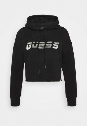 Schwarzer, verkürzter Kapuzenpullover aus Baumwolle mit einem silbernen, reflektierenden "GUESS"-Logo. Verfügt über eine Kapuze mit Kordelzug und einem kleinen grünen Akzent am Saum.