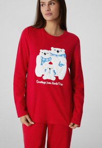 Czerwona piżama z długim rękawem z trzema białymi niedźwiedziami polarnymi w niebieskich szalikach. Pod grafiką napis "Pozdrowienia z Bieguna Północnego".