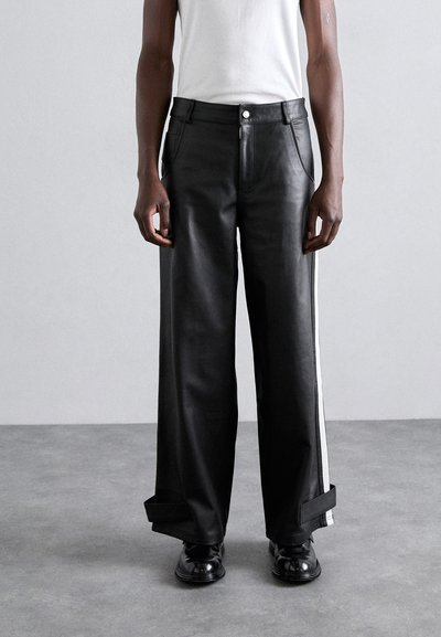 Pantalons larges en cuir noir avec une bande blanche sur le côté, dotés d'une fermeture à bouton et de revers, présentés sur un fond uni.