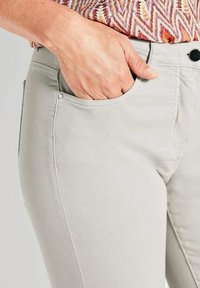 Hellgraue Hosen aus weichem Stoff, mit schlankem Design, seitlichen Taschen und sichtbaren Nähten.