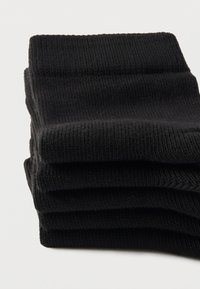 Μαύρες βαμβακερές κάλτσες στοιβαγμένες προσεκτικά, με ριμπ ύφανση και σχεδιασμό χωρίς ραφές, με μαλακό, ελαστικό μανσέτα στην κορυφή.