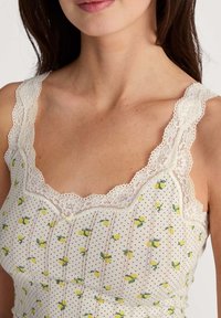 Camisole à bordure en dentelle en tissu crème avec des motifs de citrons jaunes et de feuilles vertes, accentuée par de délicates lignes ponctuées et un petit nœud.