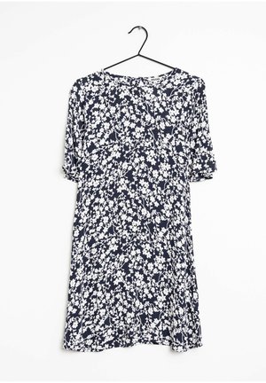 Robe bleu marine à manches courtes avec motif floral blanc suspendue sur un cintre noir sur fond blanc.