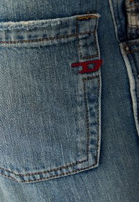 Denimske hlače v zbledeli svetlo modri barvi. Imajo zadnji žep z rdečim šivom in kontrastnim rjavim šivom ob šivih.
