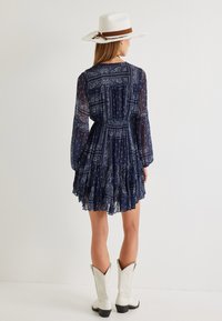 Laivansiniset, pitkähihaiset mekko paisley-kuvioilla ja röyhelöhelmalla, valmistettu kevyestä kankaasta. Yhdistetty valkoisiin cowboy-kenkään ja hattuun.