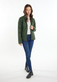 Grüne isolierte Jacke mit Reißverschluss und hohem Kragen, kombiniert mit blauen engen Jeans und schwarzen Stiefeletten. Glatte, glänzende Textur.