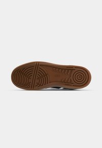 Rubber shoe sole with a brown underside, featuring textured patterns for grip and stability, surrounded by a black midsole and white accents.