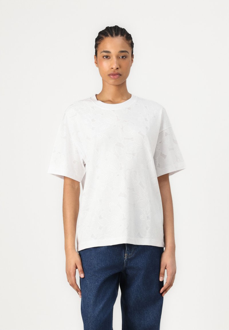 T-shirt blanc à manches courtes avec texture florale, décolleté rond et coupe décontractée. Associé à un pantalon en denim bleu foncé. Design simple et minimaliste.